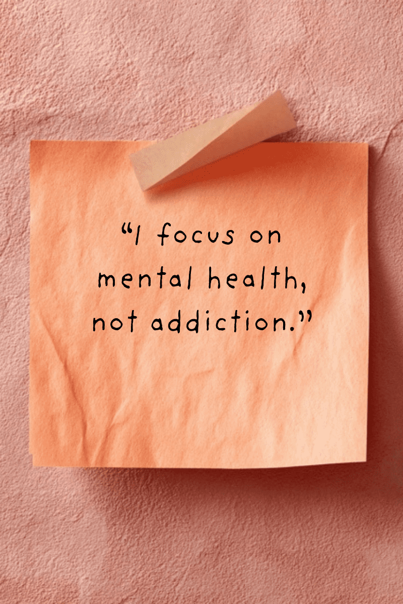 I focus on mental health, not addiction." handwritten in casual black font on an orange sticky note with a curled top edge, set on a textured coral-pink wall.