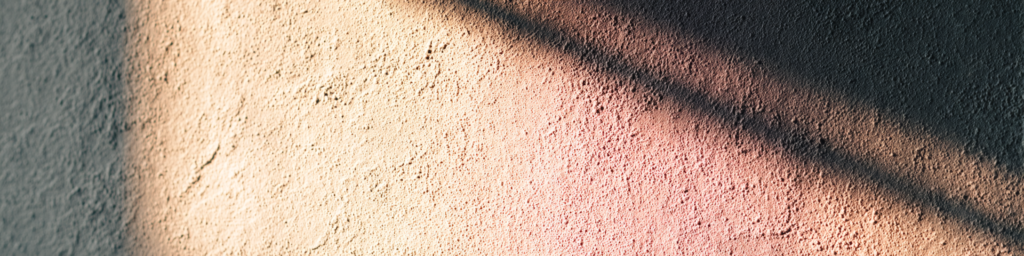 A band of warm light and shadow falling across a textured wall used as a quiet visual divider between sections